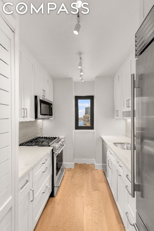 kitchen with light wood-type flooring, premium appliances, white cabinets, and tasteful backsplash