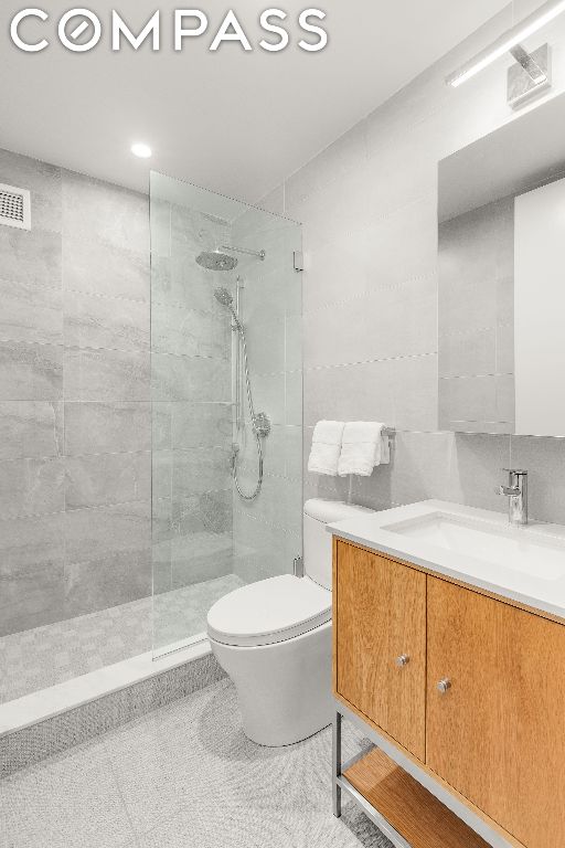 bathroom featuring toilet, vanity, and a tile shower