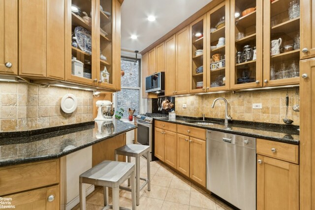 kitchen with a breakfast bar area, sink, dark stone countertops, and stainless steel appliances