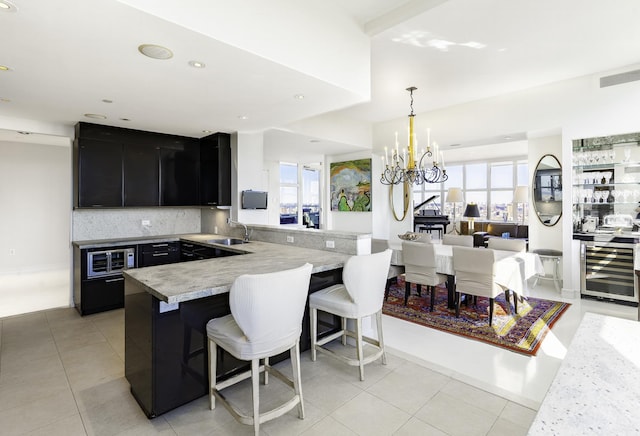kitchen featuring dark cabinets, a kitchen bar, beverage cooler, a sink, and a peninsula