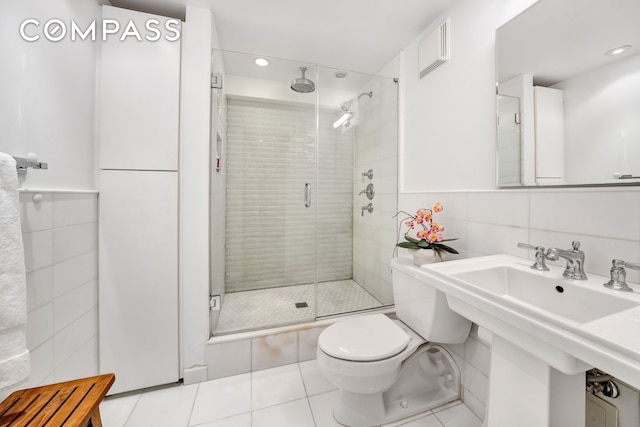 bathroom with tile walls, toilet, a stall shower, a sink, and tile patterned flooring