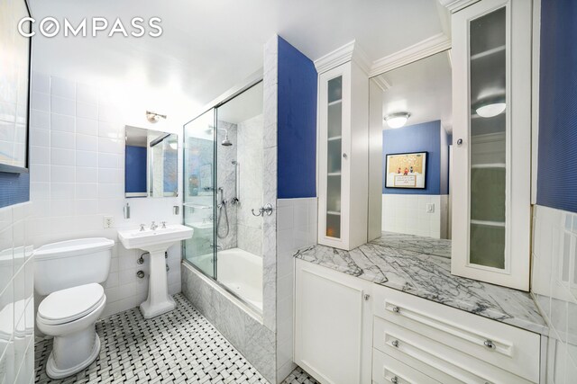 bathroom featuring tile walls, bath / shower combo with glass door, decorative backsplash, tile patterned floors, and toilet