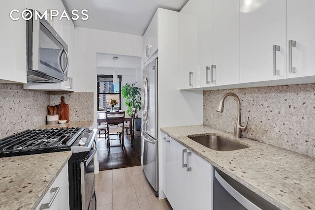 kitchen featuring decorative light fixtures, sink, white cabinets, light stone counters, and stainless steel appliances