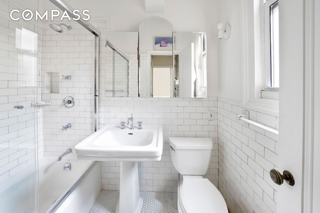 full bathroom featuring toilet, bath / shower combo with glass door, and tile walls