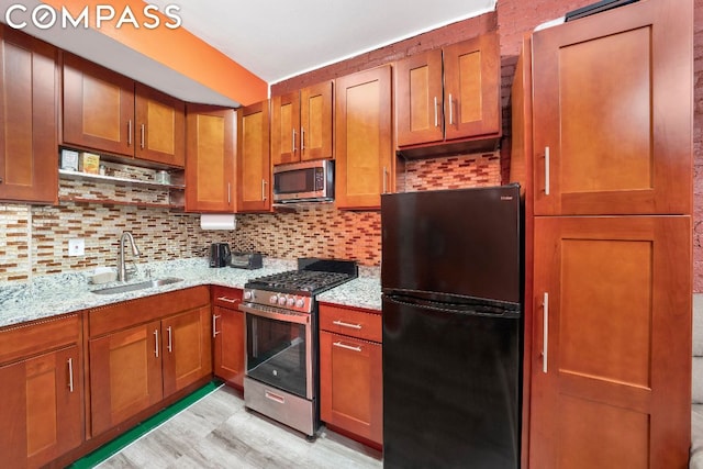 kitchen featuring appliances with stainless steel finishes, backsplash, light wood-type flooring, light stone counters, and sink