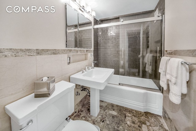 bathroom featuring toilet, bath / shower combo with glass door, and tile walls