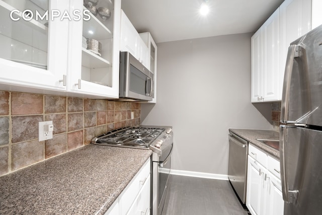 kitchen with tasteful backsplash, baseboards, white cabinets, glass insert cabinets, and appliances with stainless steel finishes