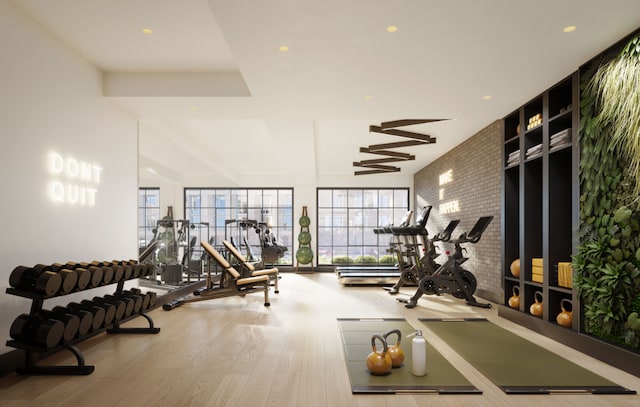 exercise room featuring brick wall and wood finished floors