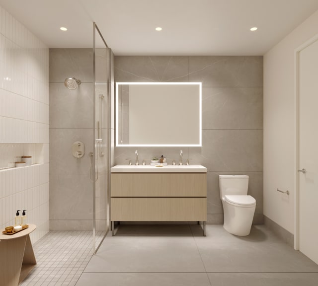 bathroom featuring tile walls, double vanity, toilet, a walk in shower, and tile patterned flooring