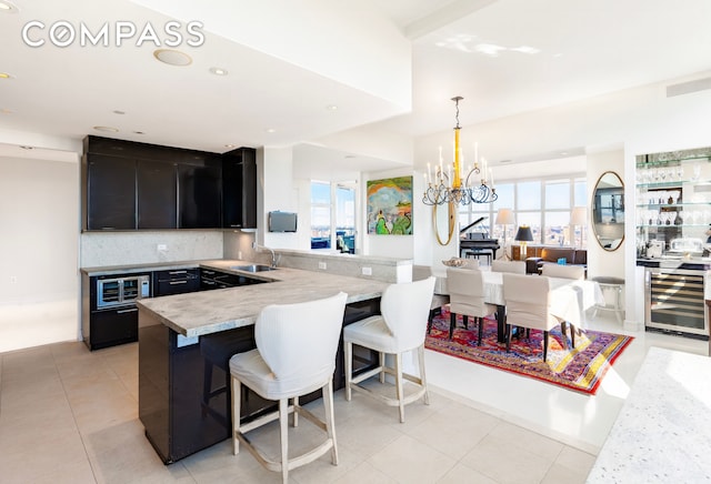 kitchen featuring dark cabinetry, a breakfast bar, beverage cooler, a sink, and a peninsula