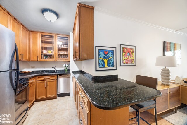 kitchen featuring dark stone counters, light tile patterned flooring, a kitchen bar, ornamental molding, and stainless steel appliances