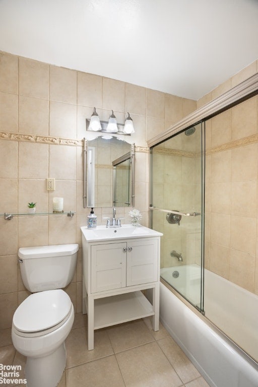 full bathroom with tile patterned flooring, tile walls, combined bath / shower with glass door, toilet, and vanity