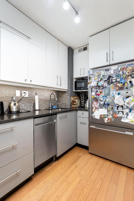 kitchen featuring dark stone countertops, decorative backsplash, white cabinetry, light wood-type flooring, and stainless steel appliances