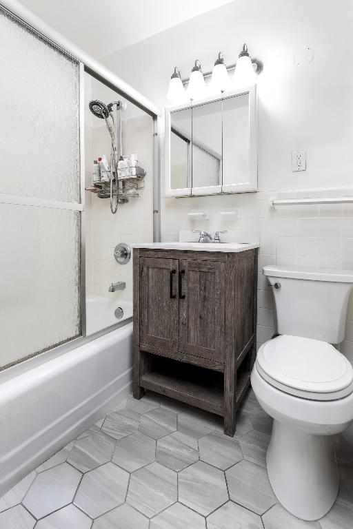 full bathroom featuring toilet, vanity, tile walls, tile patterned flooring, and shower / bath combination with glass door