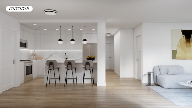 kitchen with appliances with stainless steel finishes, a kitchen island with sink, a kitchen breakfast bar, hanging light fixtures, and white cabinets