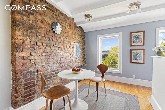 dining area with beamed ceiling, wood finished floors, baseboards, and brick wall