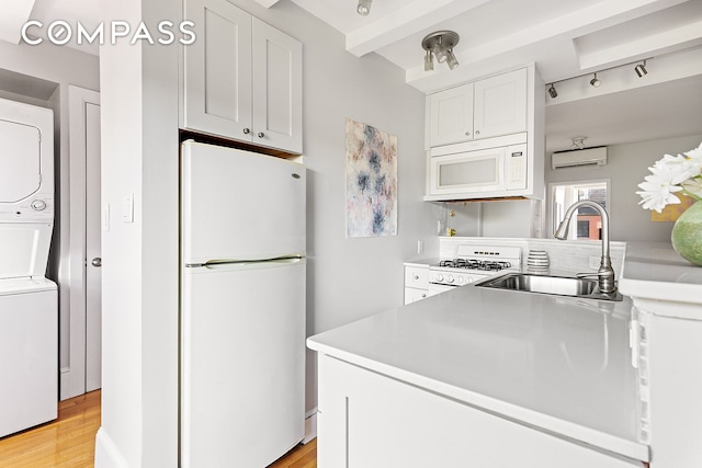 kitchen featuring an AC wall unit, a sink, white cabinetry, white appliances, and stacked washer / drying machine