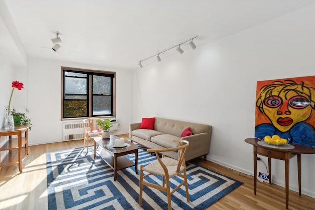 living room with radiator heating unit, track lighting, baseboards, and wood finished floors