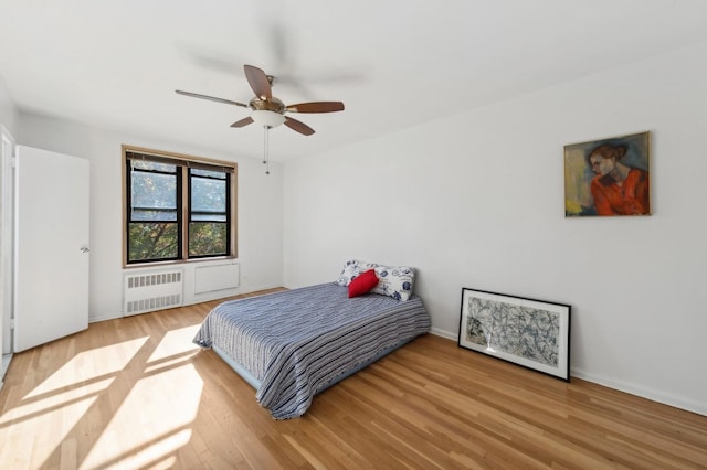 bedroom featuring radiator heating unit, wood finished floors, baseboards, and ceiling fan