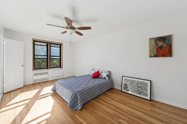 bedroom featuring radiator, wood finished floors, baseboards, and a ceiling fan