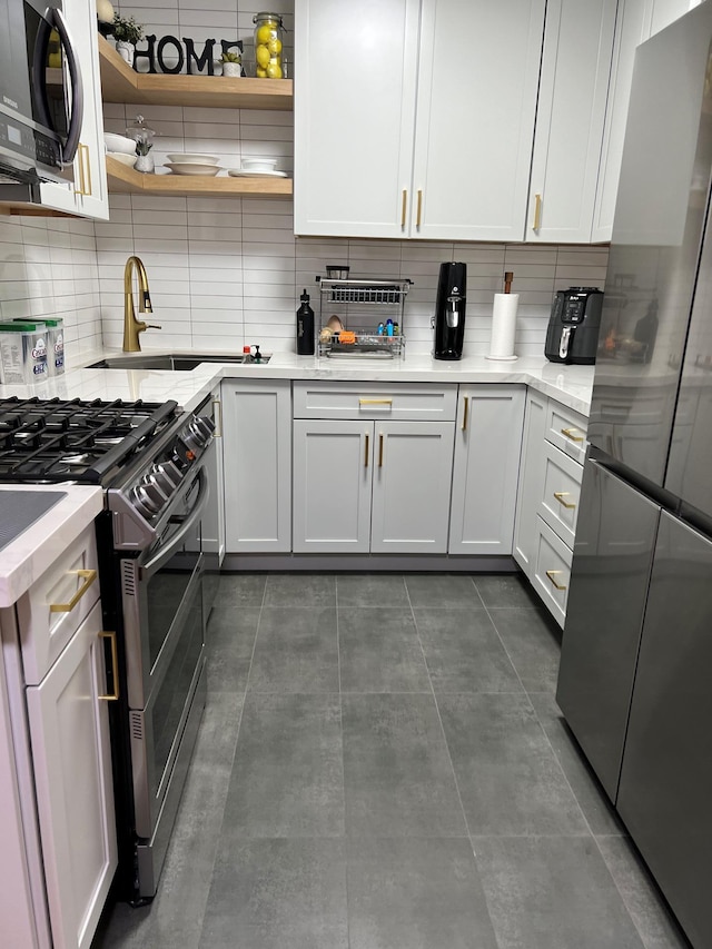 kitchen with stainless steel appliances, backsplash, white cabinetry, a sink, and dark tile patterned floors