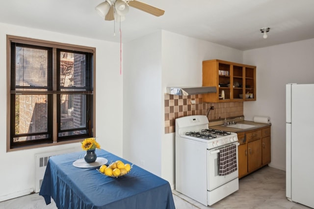 kitchen with white appliances, backsplash, a sink, brown cabinets, and ceiling fan