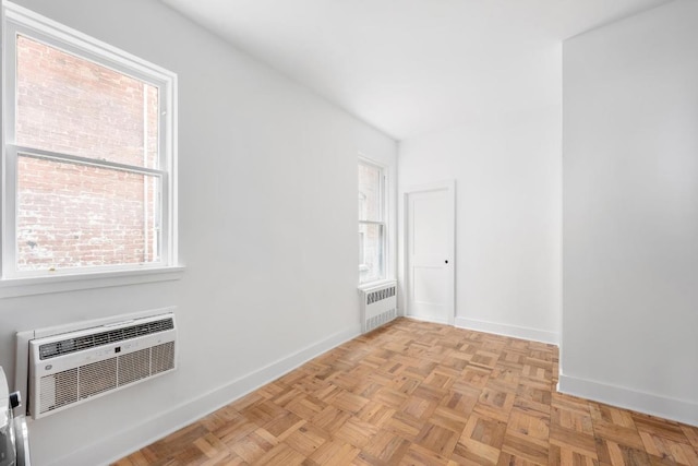 empty room featuring radiator, light parquet floors, a healthy amount of sunlight, and an AC wall unit