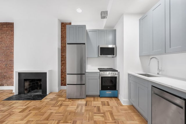 kitchen featuring brick wall, light parquet flooring, stainless steel appliances, sink, and gray cabinets