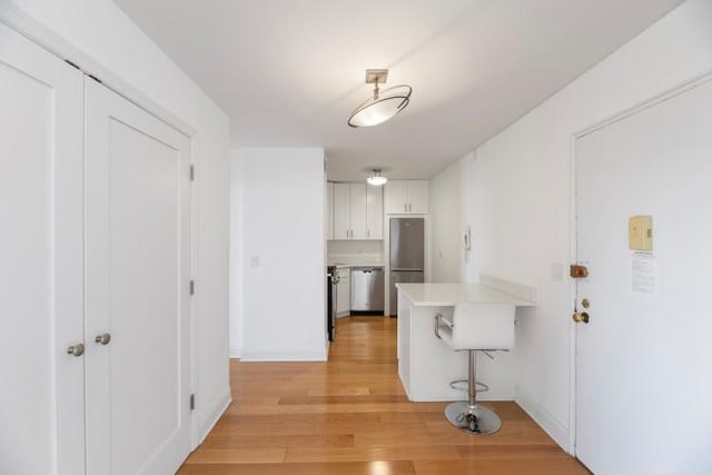 interior space with light wood finished floors, white cabinetry, a breakfast bar, a peninsula, and stainless steel appliances