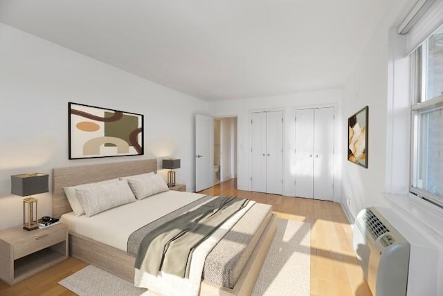 bedroom with multiple closets, a wall unit AC, and light wood finished floors