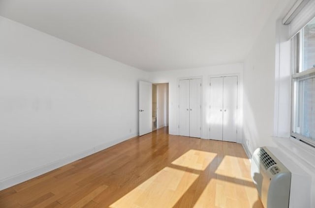 unfurnished bedroom with multiple closets, light wood-type flooring, baseboards, and a wall mounted AC