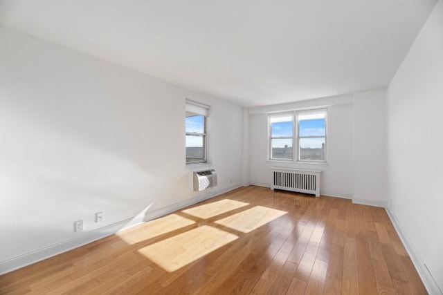 spare room with baseboards, radiator, an AC wall unit, and hardwood / wood-style flooring