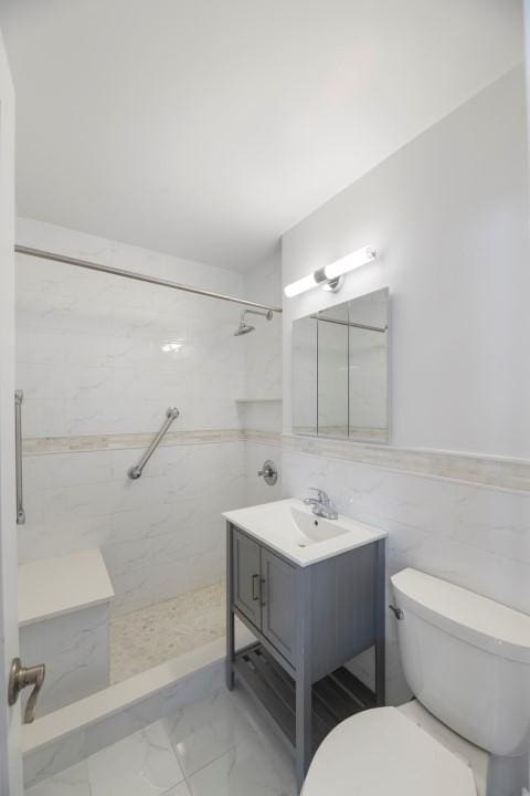 bathroom featuring marble finish floor, tile walls, toilet, vanity, and tiled shower