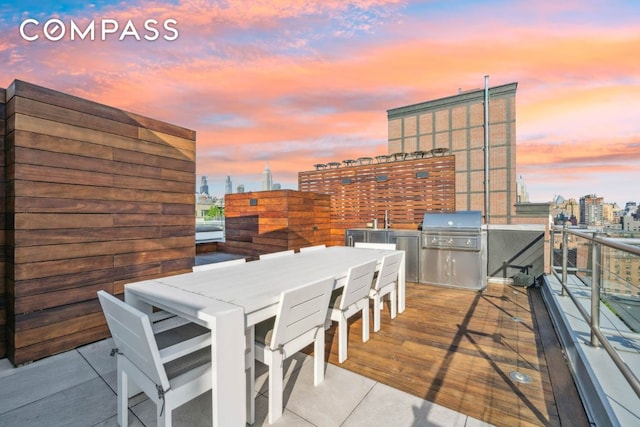 patio terrace at dusk with area for grilling, an outdoor wet bar, and exterior kitchen