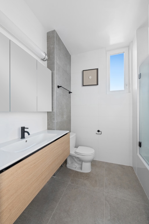 full bathroom featuring vanity, bath / shower combo with glass door, tile patterned floors, and toilet