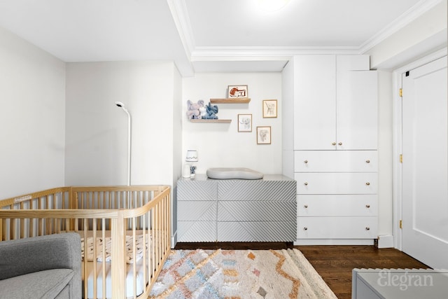 bedroom with dark wood-type flooring, a nursery area, and ornamental molding