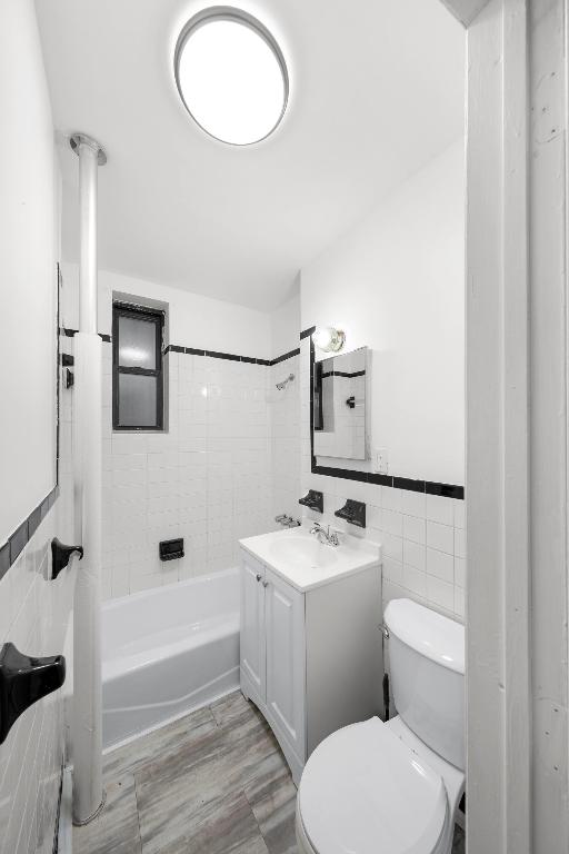 full bathroom with toilet, tile walls, tiled shower / bath, and vanity