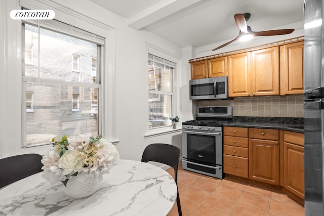 kitchen with ceiling fan, backsplash, dark stone countertops, light tile patterned flooring, and appliances with stainless steel finishes