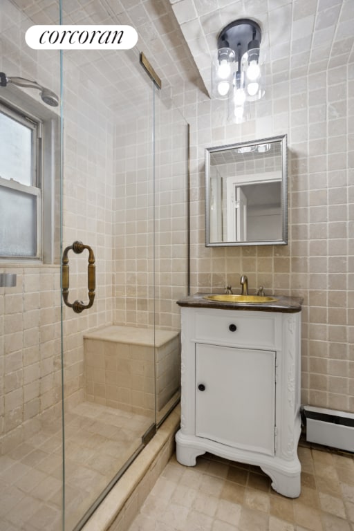 bathroom featuring a shower with shower door, vanity, tile walls, and a baseboard radiator