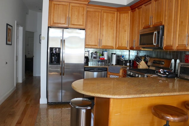 kitchen featuring backsplash, light stone countertops, brown cabinets, a kitchen breakfast bar, and stainless steel appliances