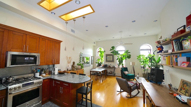 kitchen with tasteful backsplash, light wood-style floors, a peninsula, appliances with stainless steel finishes, and a skylight