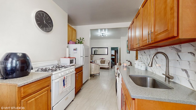 kitchen with white appliances, light stone counters, brown cabinets, a sink, and backsplash