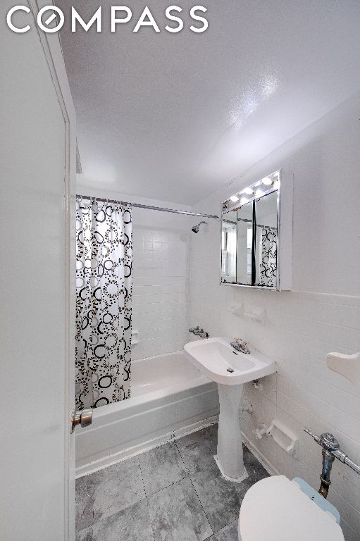 bathroom featuring tile walls, toilet, a textured ceiling, and shower / tub combo with curtain