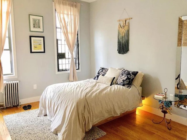 bedroom with multiple windows, hardwood / wood-style floors, and radiator