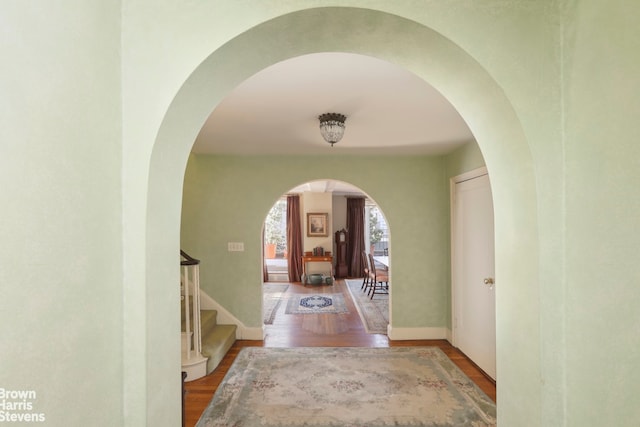 corridor with baseboards, arched walkways, wood finished floors, and stairway