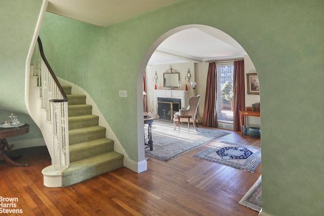 staircase with arched walkways, wood-type flooring, a fireplace, and baseboards