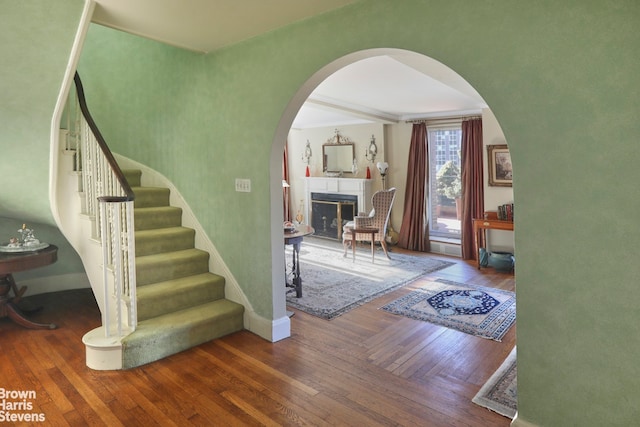 staircase featuring arched walkways, baseboards, hardwood / wood-style flooring, and a fireplace