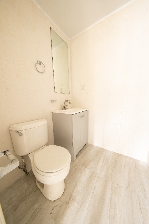 bathroom with toilet, tile walls, and vanity