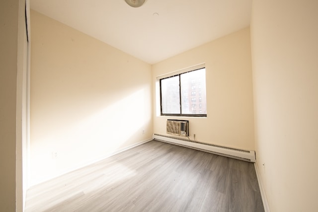 unfurnished room with an AC wall unit, a baseboard heating unit, and light wood-type flooring