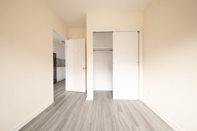 unfurnished bedroom with a closet, light hardwood / wood-style flooring, and black refrigerator